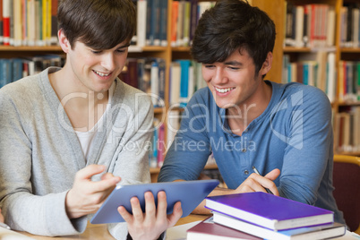 Students sitting at library desk looking at tablet pc