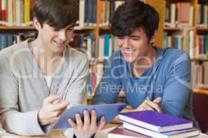 Students sitting at library desk looking at tablet pc