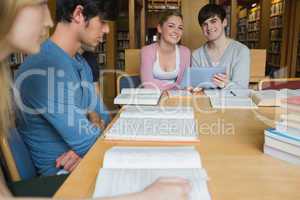 Students sitting at library table smiling while holding a tablet