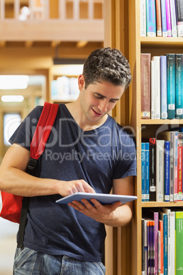 Man leaning at a bookshelf while holding a tablet pc