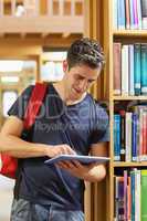 Man leaning at a bookshelf while holding a tablet pc