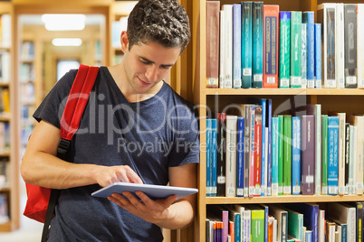 Student leaning against bookshelf holding a tablet pc