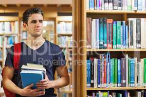 Student standing at the library holding pile of books