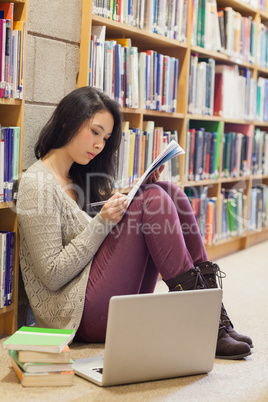 Student leaning at the wall sitting on library floor