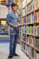 Student standing at a bookshelf smiling holding a tablet pc