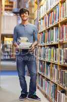 Man standing at a bookshelf holding a pile of books