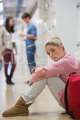 Sad student sitting against lockers