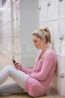 Smiling woman sitting against lockers texting