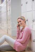 Woman sitting on the floor against lockers phoning while smiling