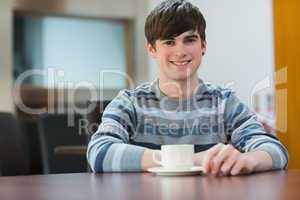 Student sitting at table drinking coffee in college cafe
