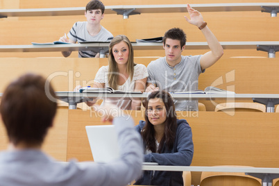 Students sitting at the lecture hall with man razing hand to ask
