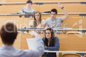 Students sitting at the lecture hall with man razing hand to ask