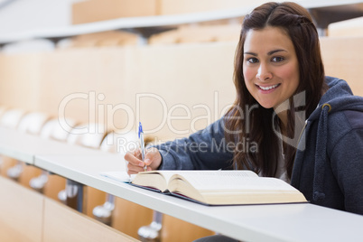Girl sitting smiling while reading a book and taking notes