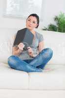 Thoughtful woman sitting on a couch with notepad