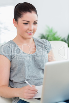 Young woman on the couch using a laptop and taking notes