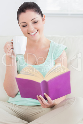Woman sitting on the couch while reading and drinking