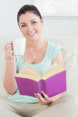 Woman sitting on the couch and reading while drinking