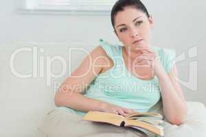 Thoughtful woman reading a book on the couch