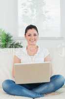 Smiling woman using a laptop and sitting on the couch