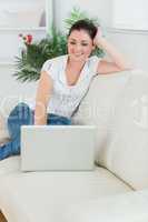 Woman sitting on the couch and smiling while using a laptop