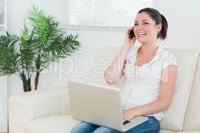 Phoning woman on the couch using a laptop