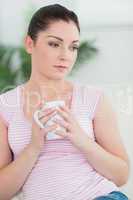 Thoughtfully woman sitting on the couch holding a mug