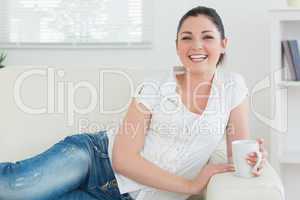 Woman relaxing while lying on the couch and holding a cup