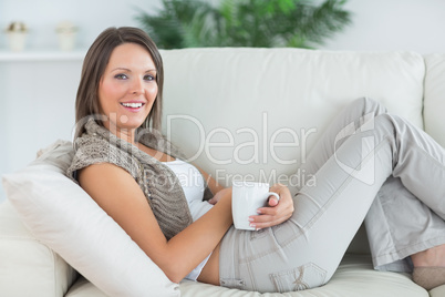 smiling woman lying on the sofa and holding a mug