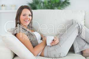 smiling woman lying on the sofa and holding a mug