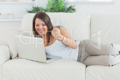 Happy woman using her laptop and lying on sofa