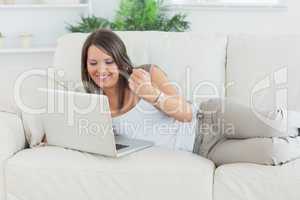 Happy woman using her laptop and lying on sofa
