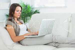 Serious woman lying on the sofa and using her laptop