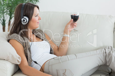 Woman lying on the sofa and listening to music with a red wine g