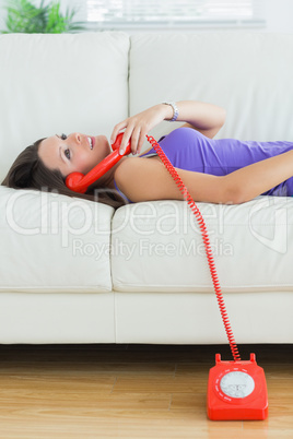 Happy woman using her land line and lying on sofa