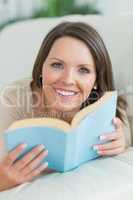 Woman lying on sofa looking happy with a book