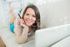 smiling woman using her laptop lying on sofa