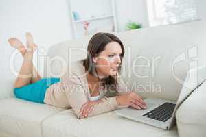 Brunette lying on sofa and using her laptop