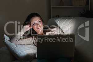 Woman lying on sofa with her laptop in night