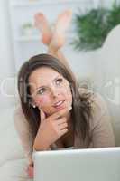 Thoughtful woman lying on the sofa with her laptop