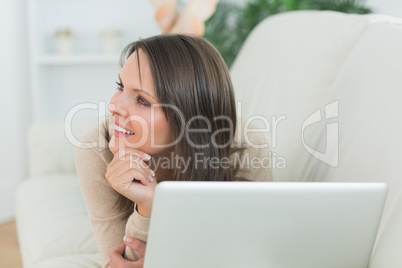 Woman lying on sofa looking away with her laptop