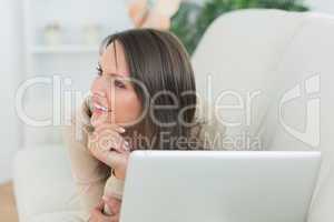 Woman lying on sofa looking away with her laptop