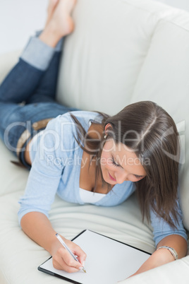 Smiling woman lying on sofa and writing