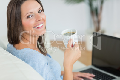 Brunette using her laptop and drinking a cup of coffee