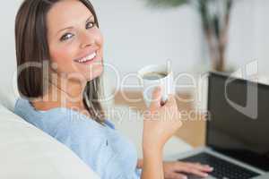 Brunette using her laptop and drinking a cup of coffee