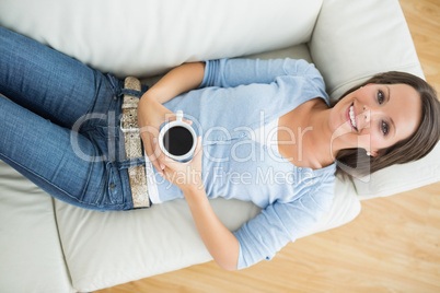 Smiling woman holding a mug of coffee on sofa