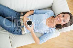 Smiling woman holding a mug of coffee on sofa
