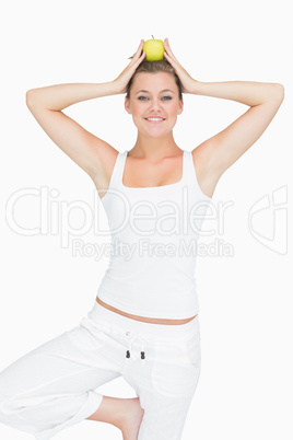 Woman doing yoga pose holding apple on her head