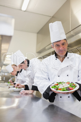 Cheerful chef showing his salad with workers in background