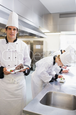 Chef presenting desert with others working on deserts