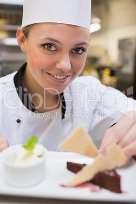 Smiling chef garnishing a slice of cake with wafers